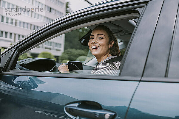Glückliche junge Frau  die durch das Autofenster auf die Straße blickt