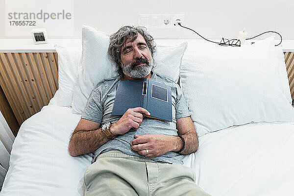 Senior man sleeping with book on bed at home