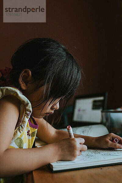 Vorschulkind malt zu Hause mit geöffnetem Laptop