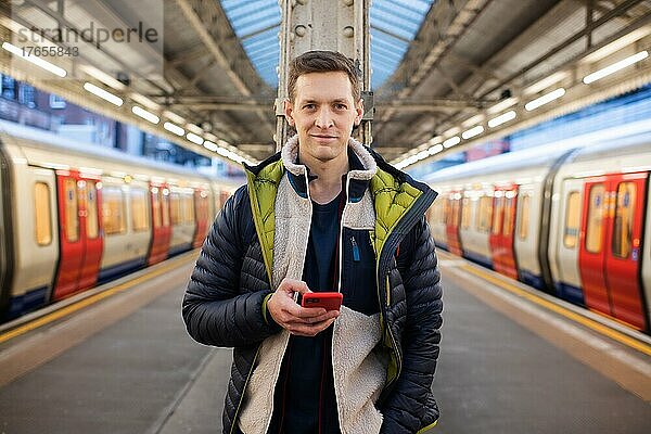 Mann steht auf einem Bahnsteig und schaut auf sein Telefon und wartet auf einen Zug