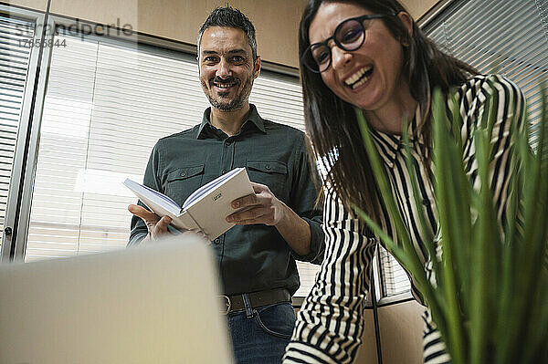 Männer und Frauen mittleren Alters lachen  während sie in einem Büro arbeiten.
