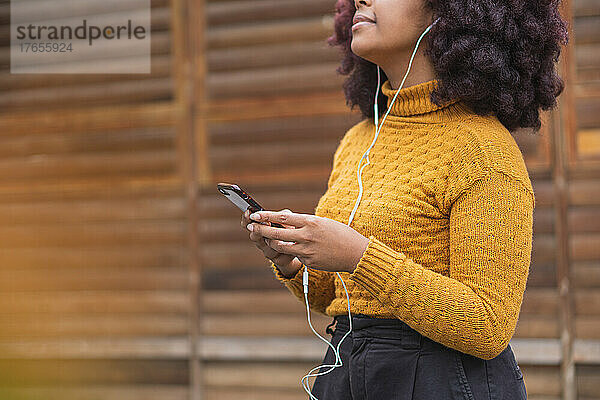 Junge Afro-Frau hört Musik auf ihrem Mobilgerät.