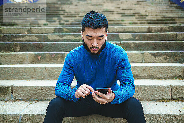 Ernsthafter ethnischer Mann benutzt Smartphone auf Steintreppe