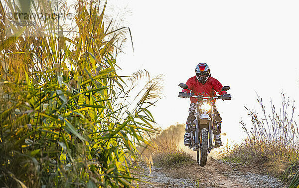 Mann fährt mit seinem Scrambler-Motorrad durch unwegsames Gelände in Thailand