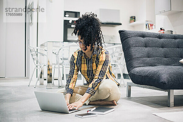 Junge Afro-Frau arbeitet von zu Hause aus und sitzt mit ihrem Laptop auf dem Boden
