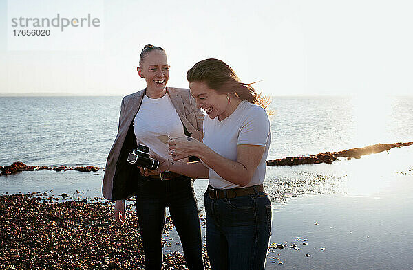 Lesbisches Paar  das am Strand lacht und Selfies macht