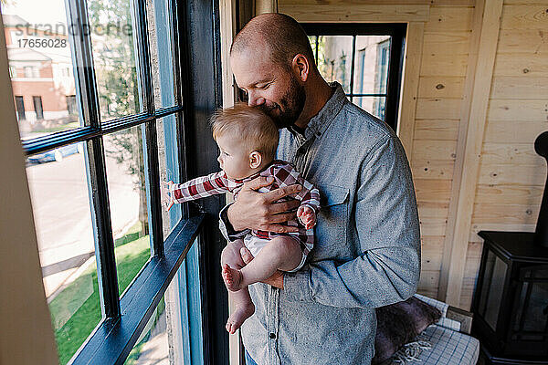 Der liebevolle Vater küsst das kleine Mädchen auf den Kopf  während es durch das Fenster schaut