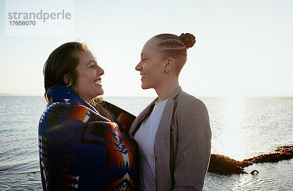 Lesbisches Paar lacht gemeinsam am Strand bei Sonnenuntergang