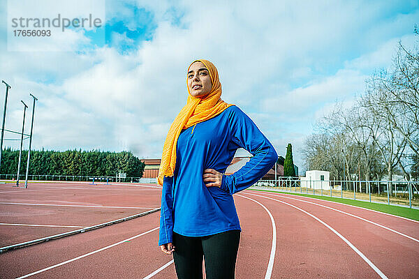 Lächelnde arabische Frau  die während des Trainings auf dem Leichtathletikfeld steht