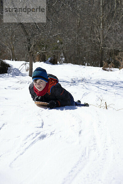 Junge rutscht vom Schneehang herunter.