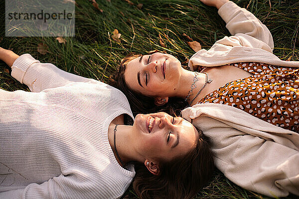 Zwei glückliche Mädchen im Teenageralter lächeln  während sie mit geschlossenen Augen im Gras liegen