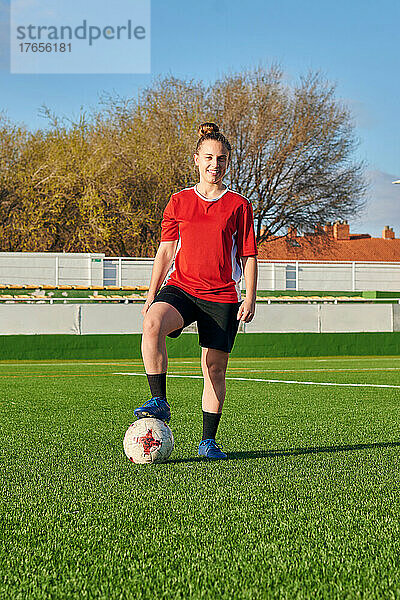 Eine Fußballspielerin posiert mit einem Fußball und blickt in die Kamera