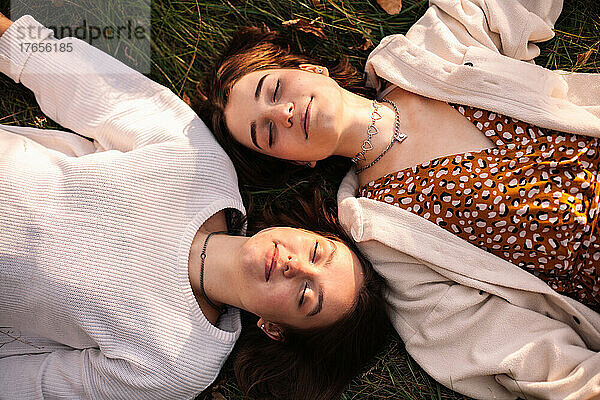 Draufsicht auf zwei glückliche junge Frauen  die mit geschlossenen Augen im Gras liegen