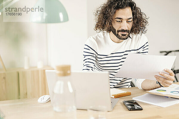 Junger Mann arbeitet im modernen Büro mit Laptop und hält Papiere in der Hand