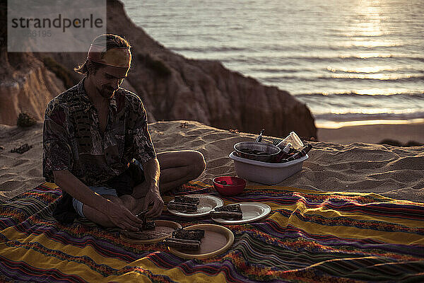 Ein reisender Mann bereitet bei Sonnenuntergang ein Picknick am Meer vor