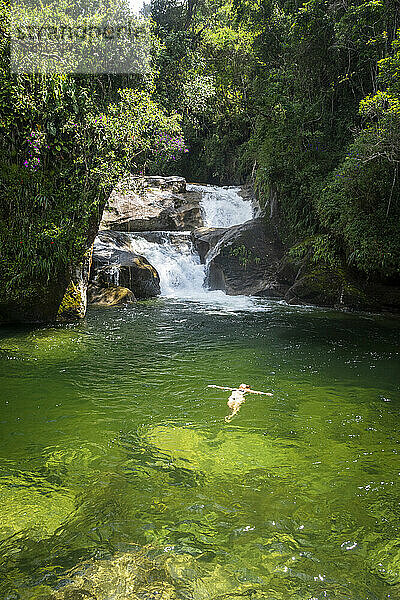 Schöne Aussicht auf eine Frau  die im grünen Pool am Regenwaldwasserfall schwimmt