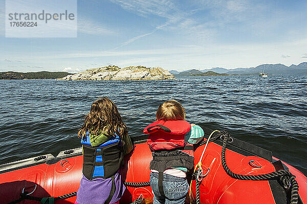 Zwei kleine Kinder schauen über den Bug eines Schlauchbootes in einer großen Bucht