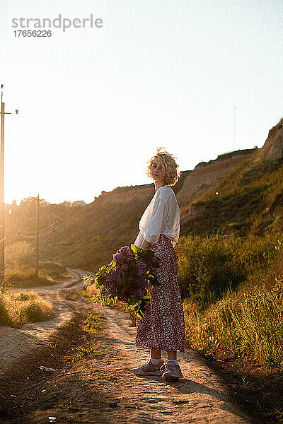 Blonde Frau in weißer Bluse bei Sonnenuntergang mit Gebläsen