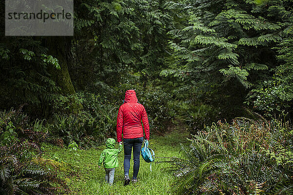 Eine Frau im Regenmantel geht mit einem kleinen Kind in den Wald