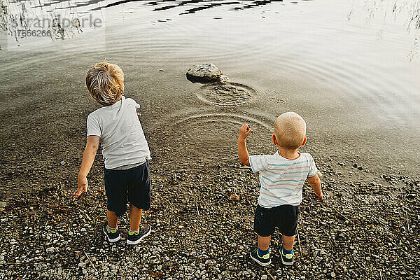 Rückansicht von Kindern  die im Sommer Kieselsteine ??ins Wasser werfen