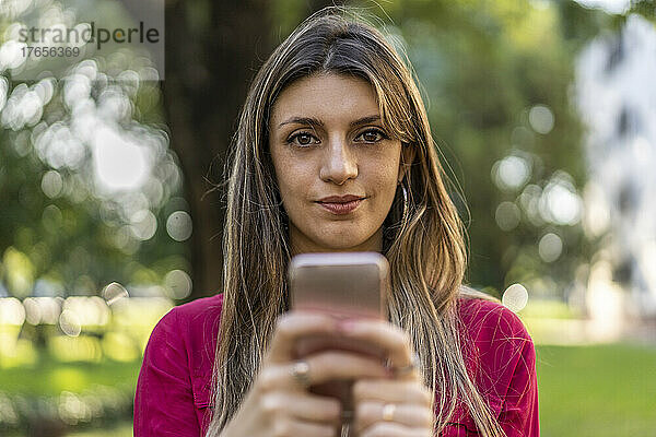 Eine Frau benutzt ihr Smartphone im Freien. Sie blickt in die Kamera.