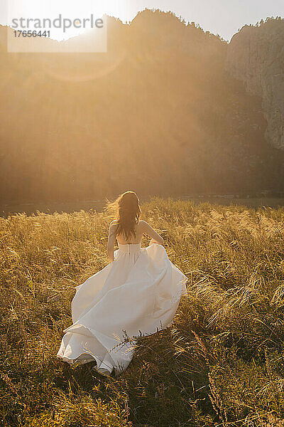 Eine Braut im Hochzeitskleid rennt bei Sonnenuntergang durch das Gras