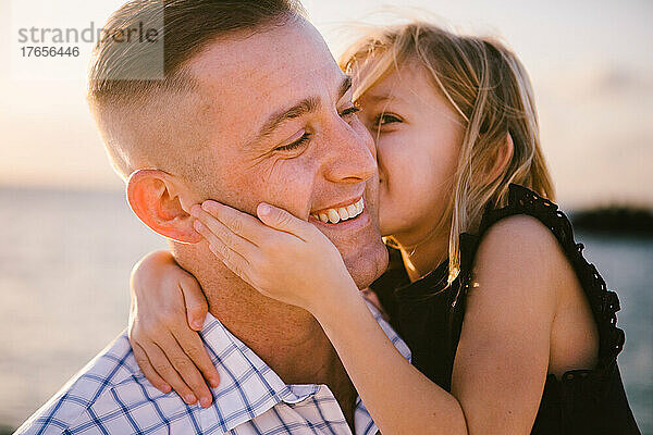 5-jährige Tochter gibt Vater am Meer einen Kuss auf die Wange