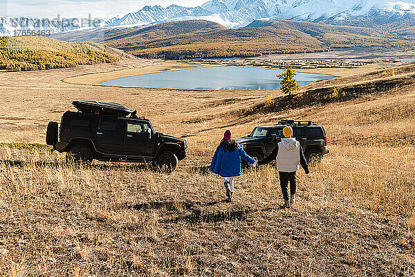 Ein paar verliebte Männer fahren zu zwei schwarzen SUVs vor dem Hintergrund eines Sees