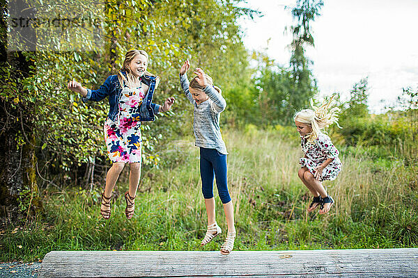 Drei schöne junge Mädchen springen und spielen draußen.