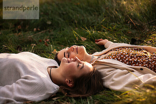 Glückliches lesbisches Paar lächelt  während es mit geschlossenen Augen im Gras liegt