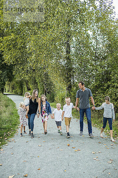 Achtköpfige Familie hält Händchen beim Spazierengehen im Naturpark.