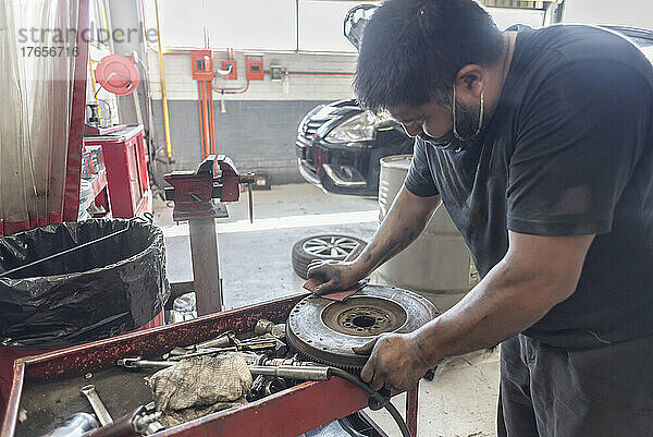 Lateinamerikanischer Mechaniker schleift eine gebrauchte Kupplungsscheibe in einer Werkstatt