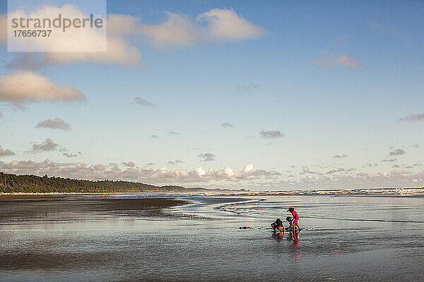 Drei Kinder spielen bei Sonnenuntergang im Sand an einem breiten Strand