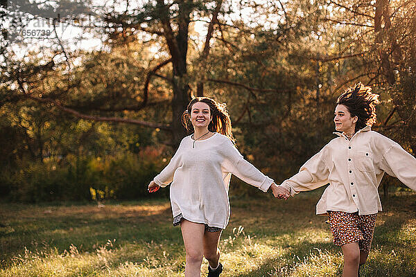 Zwei glückliche Freundinnen halten sich beim Laufen im Wald an den Händen