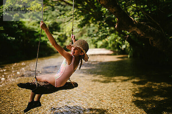 Junges Mädchen auf Baumschaukel über einem Fluss im Sommer