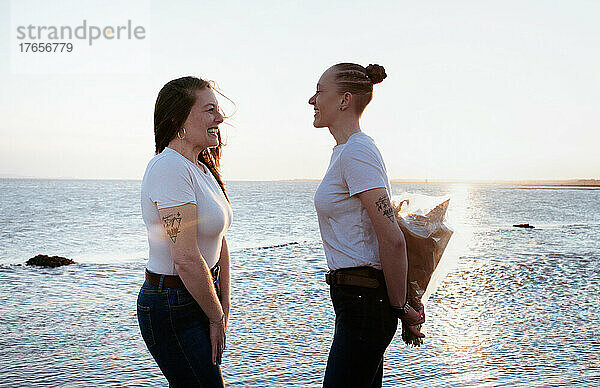 Lesbisches Paar  das am Strand einen Blumenstrauß schenkt