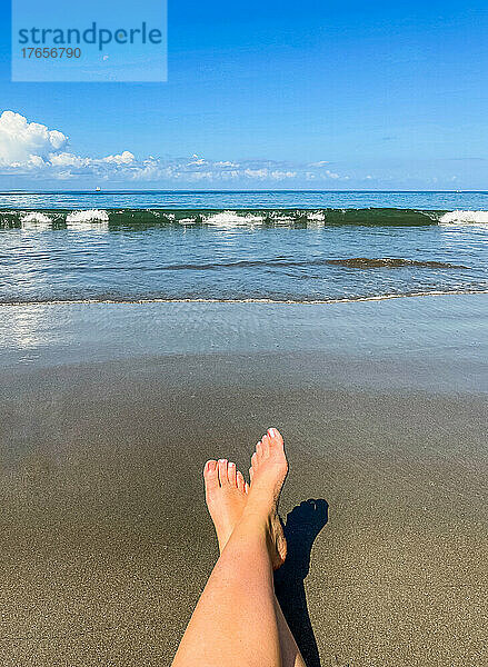 Die ausgestreckten Füße einer Frau entspannen sich am Strand am Meer.