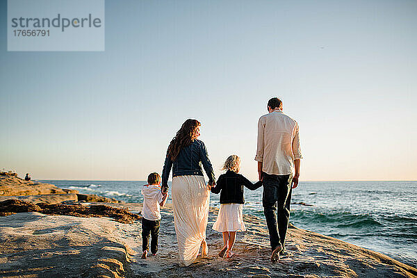 Vierköpfige Familie spaziert bei Sonnenuntergang in San Diego an einer Klippe am Strand entlang