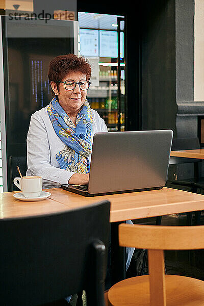 Reife Frau arbeitet remote mit ihrem Laptop in einem Café