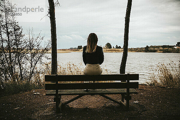 Unerkennbares trauriges Mädchen  das auf einer Bank sitzt und auf einen See blickt