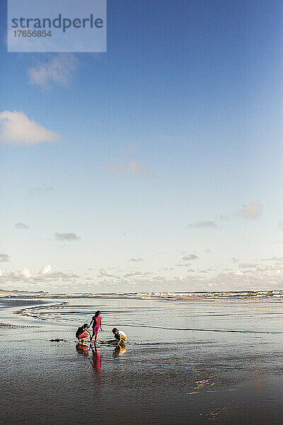 Drei Kinder spielen im Sand an einem leeren  sonnigen Strand