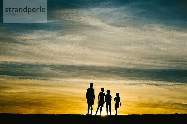 Vier Geschwister-Silhouetten bei goldenem Sommersonnenuntergang