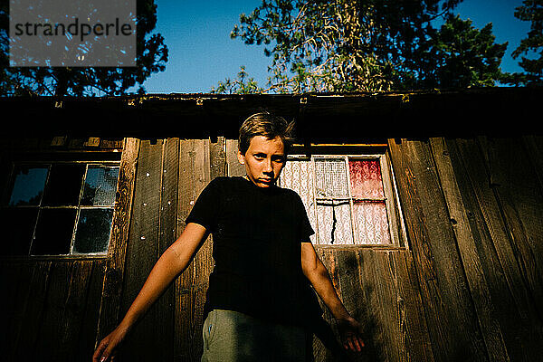 Teen Boy Stares Intensely into Camera at Golden Hour Next to Old Shed