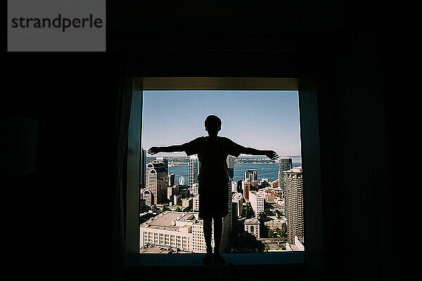 Silhouette eines Jungen im Hotelfenster vor dem Stadtbild