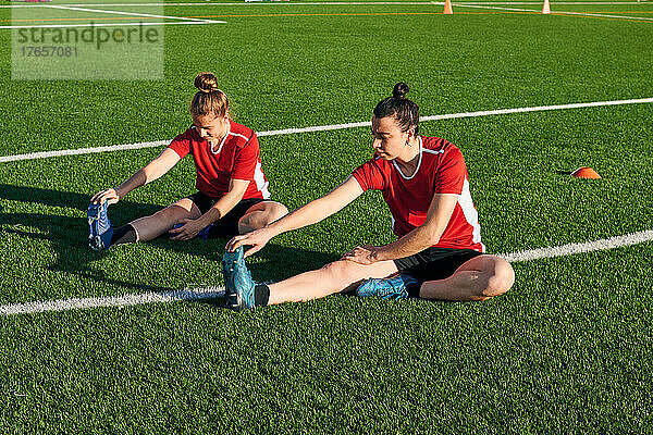 Zwei Fußballspielerinnen dehnen sich während einer Trainingseinheit