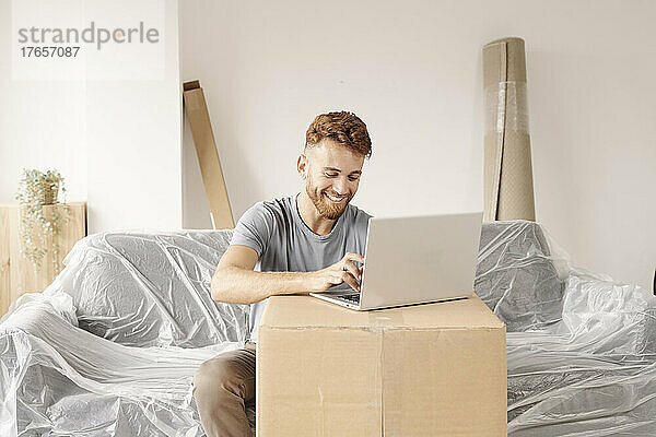 Ein fröhlicher junger Mann sitzt auf der Couch in seinem neuen Zuhause.