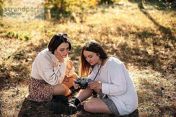 Freundinnen mit Kamera sitzen im Herbst auf Gras im Park