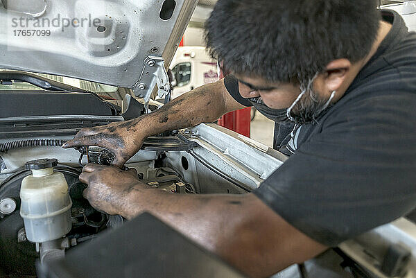 Lateinischer männlicher Mechaniker  der in einer Werkstatt die Sicherungen eines Autos überprüft