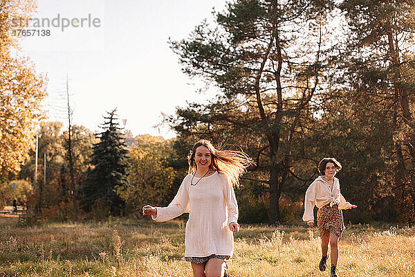 Zwei glückliche Mädchen im Teenageralter lächeln beim Laufen im Wald im Herbst