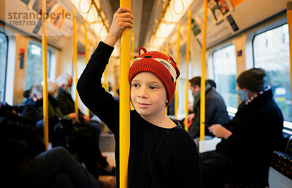 Junge steht in einem Zug in London  umgeben von Passagieren